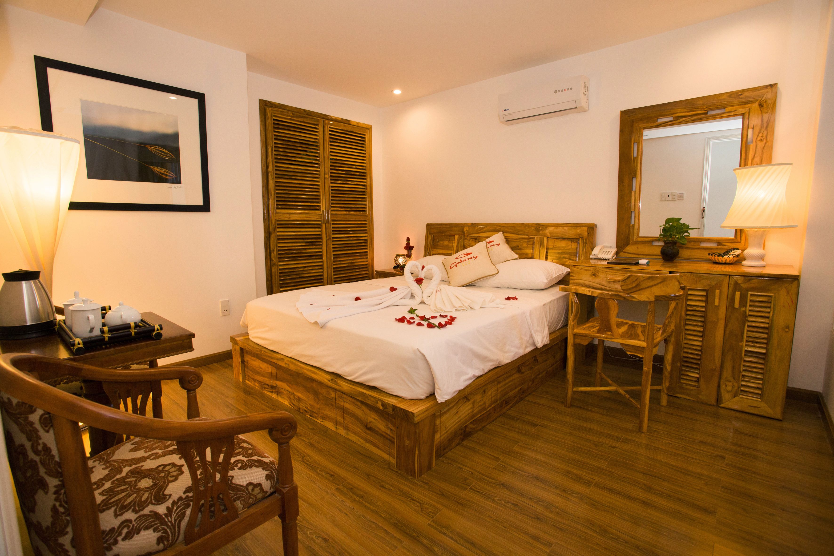 A neatly arranged bedroom with a wooden bed, a desk, a chair, and a bedside table with a lamp.