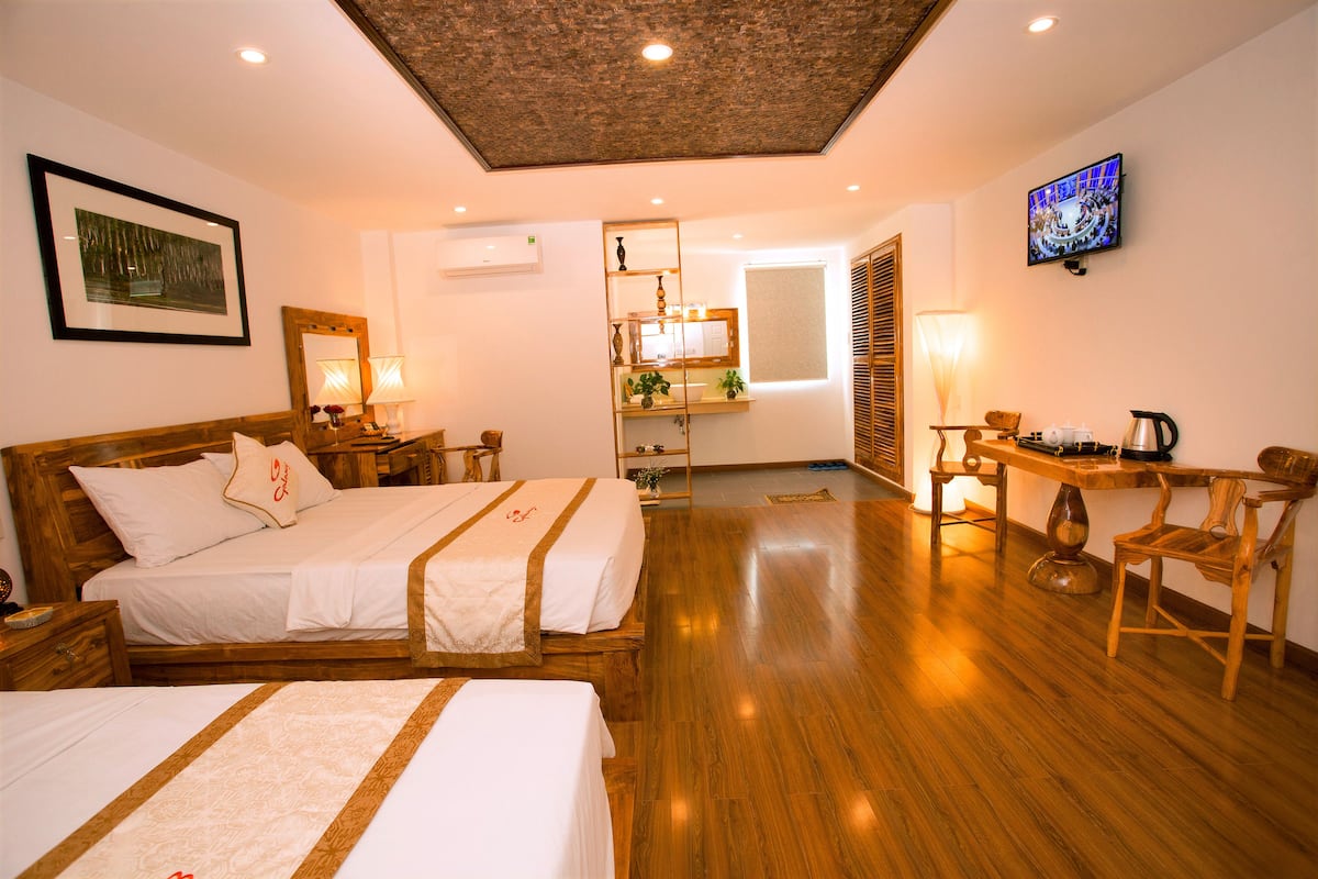 A hotel room with a wooden bed, a desk with a chair, a television, and a bathroom visible through a door.