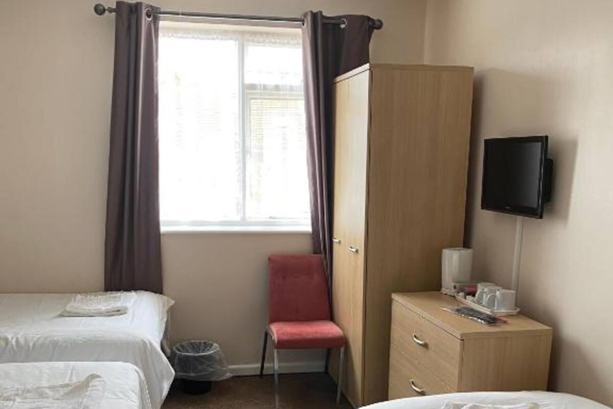 Une chambre d’hôtel avec deux lits, une chaise, un bureau, une télévision et une fenêtre avec des rideaux.