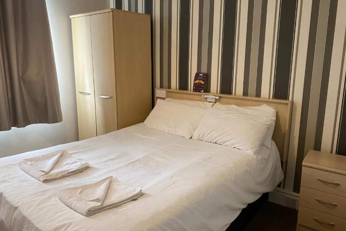 Un lit bien fait, avec du linge de lit blanc et deux serviettes pliées au pied du lit.
