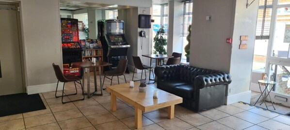 Een hal met een zwarte leren bank, een houten bijzettafeltje en twee stoelen. Achterin staan ​​arcadekasten.
