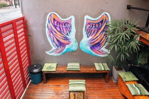 A wooden deck with a bench, a trash bin, and a wall with a colorful mural. - Soul Hostel (São Paulo)
