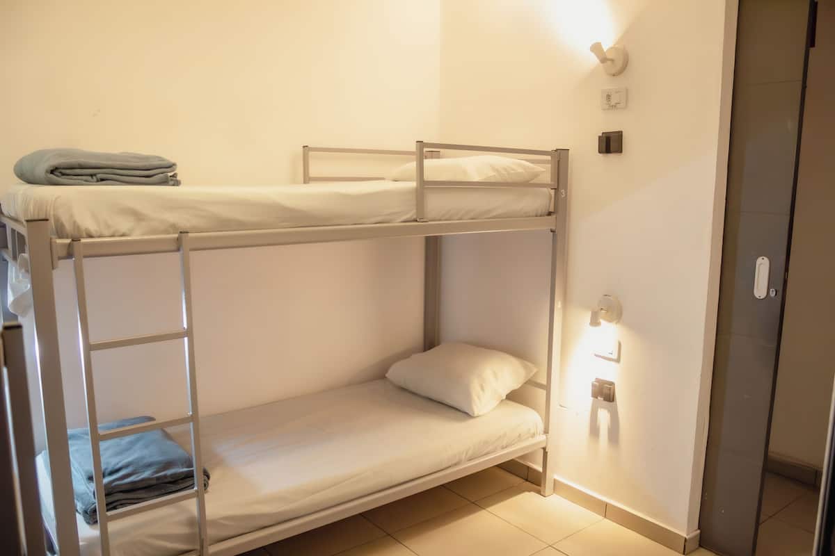 Habitación con literas, una litera inferior, una escalera, una manta doblada y una lámpara fijada a la pared.