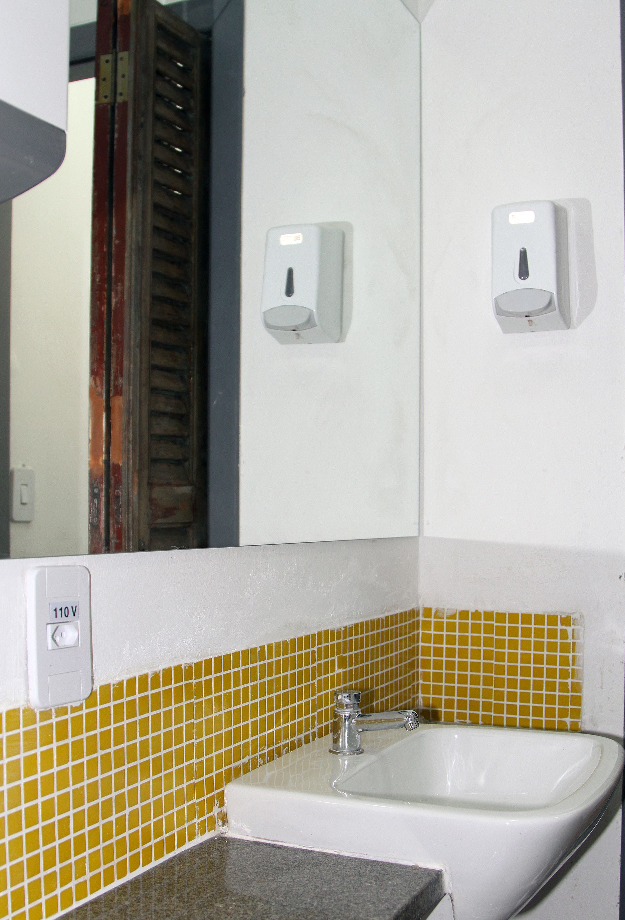 A bathroom with a white sink, yellow-tiled walls, and a mirror.