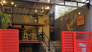 Entrada de restaurante con escaleras, contraventanas rojas y mesas al aire libre.