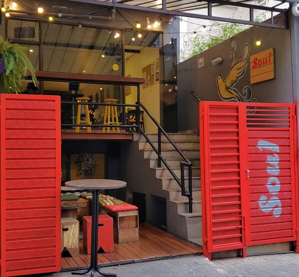 A restaurant entrance with a staircase, red shutters, and outdoor seating.