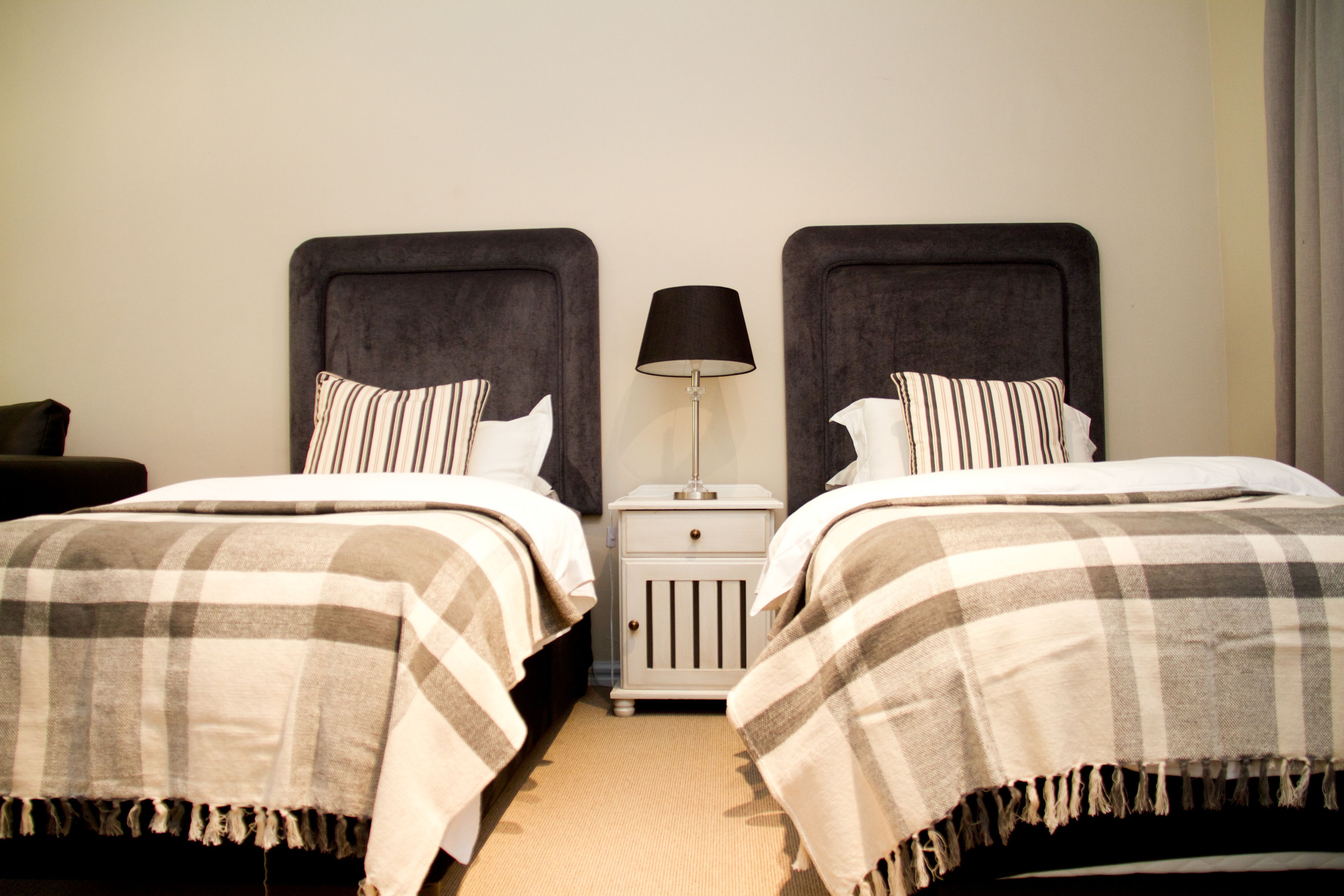 Een hotelkamer met twee bedden, elk met een hoofdbord, een nachtkastje met een lamp en een gestreept kussen.