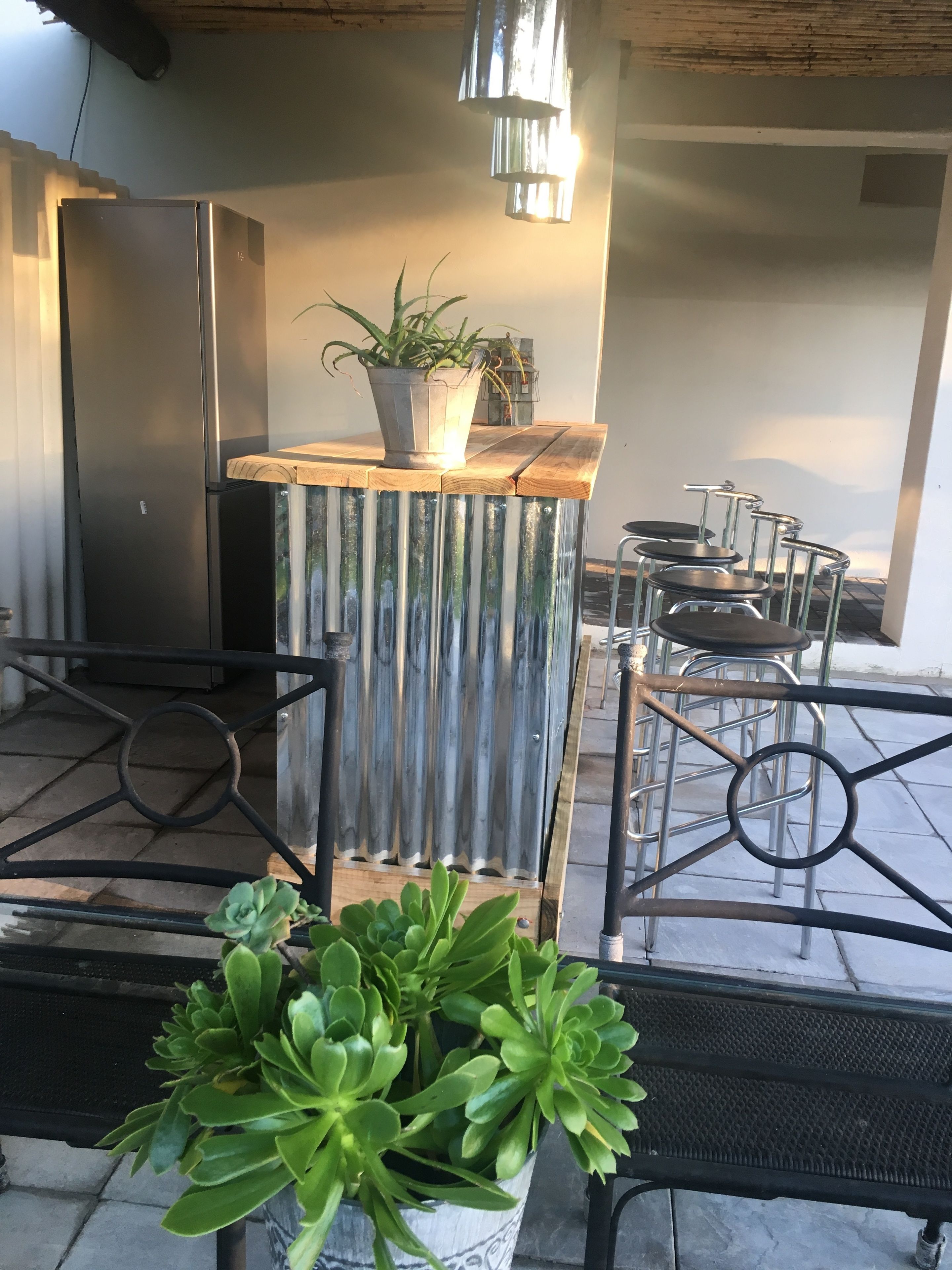 A modern outdoor seating area with metal chairs and a table, a potted plant, and a refrigerator.