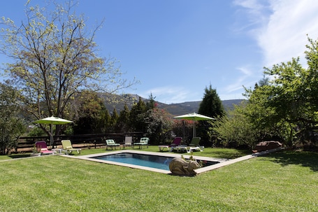 Una piscina al aire libre, sombrillas, sillones reclinables de piscina