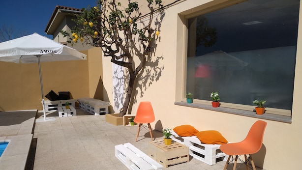 An outdoor seating area with white plastic furniture, orange chairs, and a white umbrella labeled "AMSTEL". - Hostal L´Esplai (Viladamat)