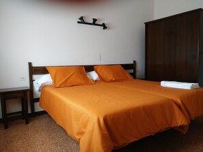 Un lit simple avec une couvre-lit et des oreillers orange, une tête de lit en bois, une table de chevet, une armoire et un luminaire fixé au mur.