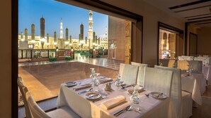 A dining area with tables set for four, overlooking a mosque with illuminated minarets. - Golden Tulip Al Zahabi (Madinah)