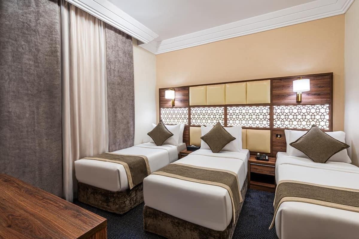 Ein Hotelzimmer mit zwei Einzelbetten, einem Holznachttisch, einem Schreibtisch und einem großen Fenster mit Vorhängen.