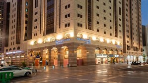 A high-rise hotel with multiple floors, large windows, and a prominent entrance with illuminated signage. - Golden Tulip Al Zahabi (Madinah)