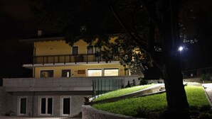 A building with a flat roof, a stone retaining wall, and a paved driveway. - Affittacamere Rubino (Ponte nelle Alpi)