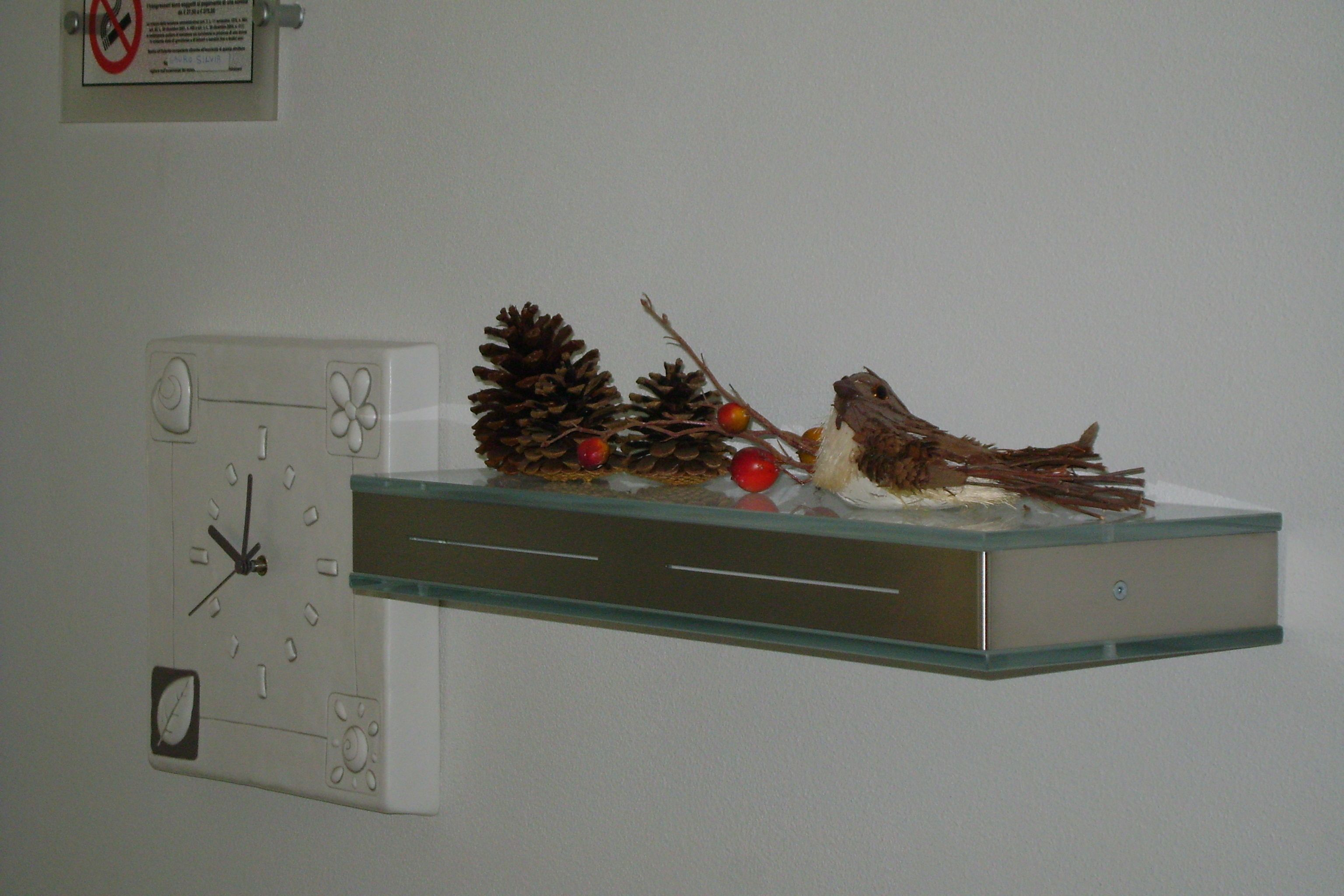 A wall clock with a pine branch and red berries on a shelf.