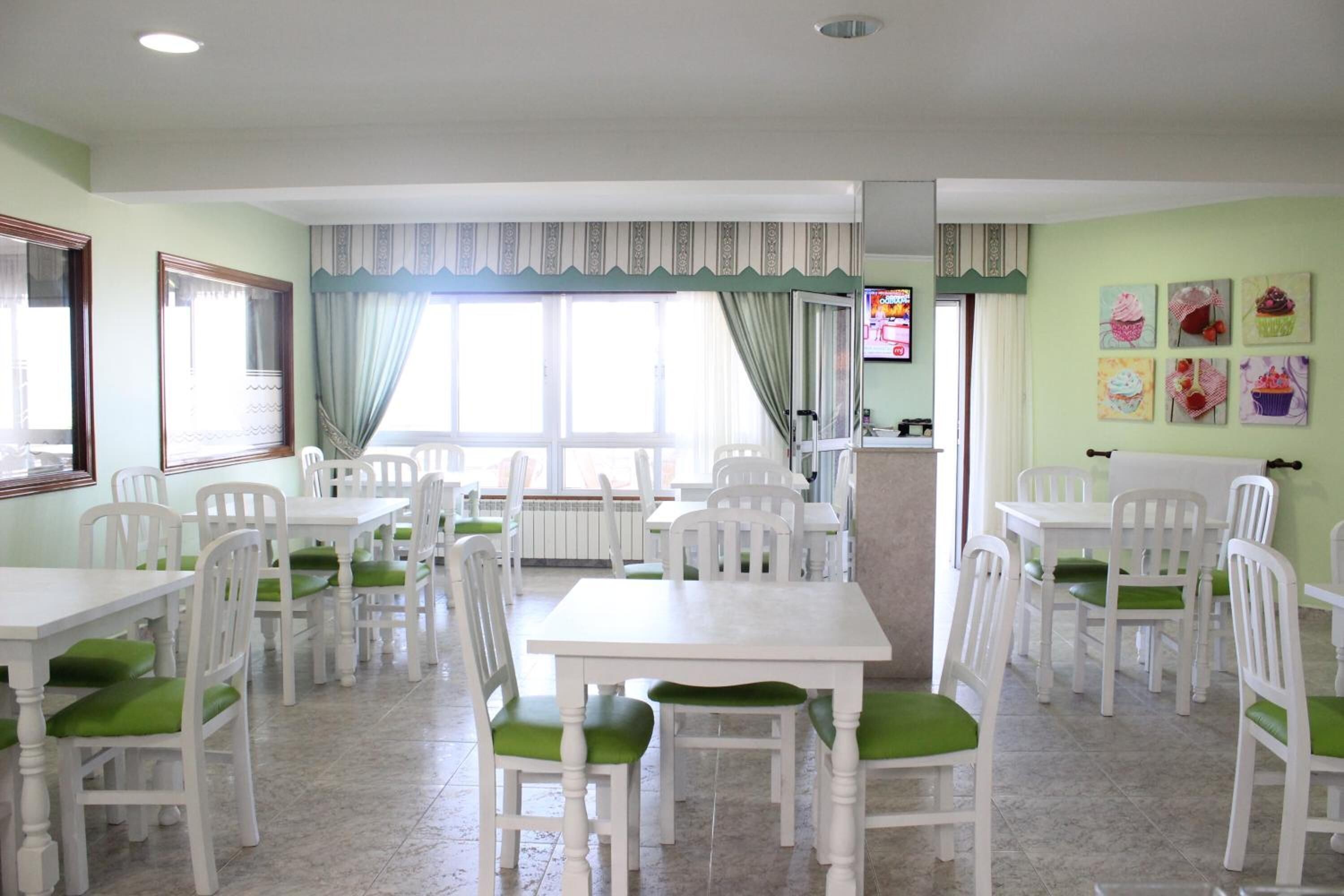 Un espace repas avec des tables et des chaises blanches, des coussins verts et un téléviseur fixé au mur.