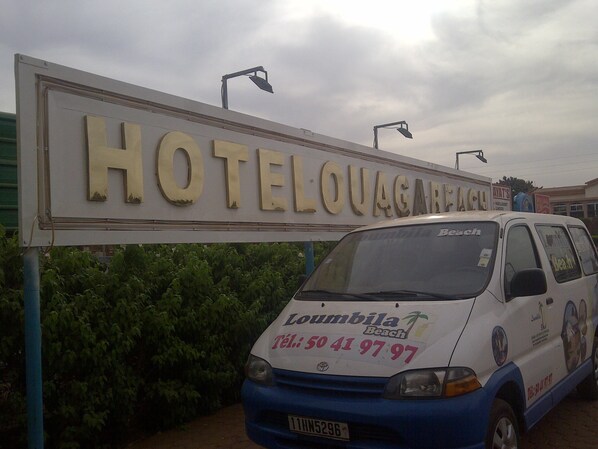 Une enseigne indiquant « HOTELLOUGAGAREACH », avec un fourgon blanc devant.