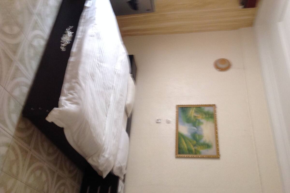 A bedroom with a bed, a wall-mounted light, and a framed picture.