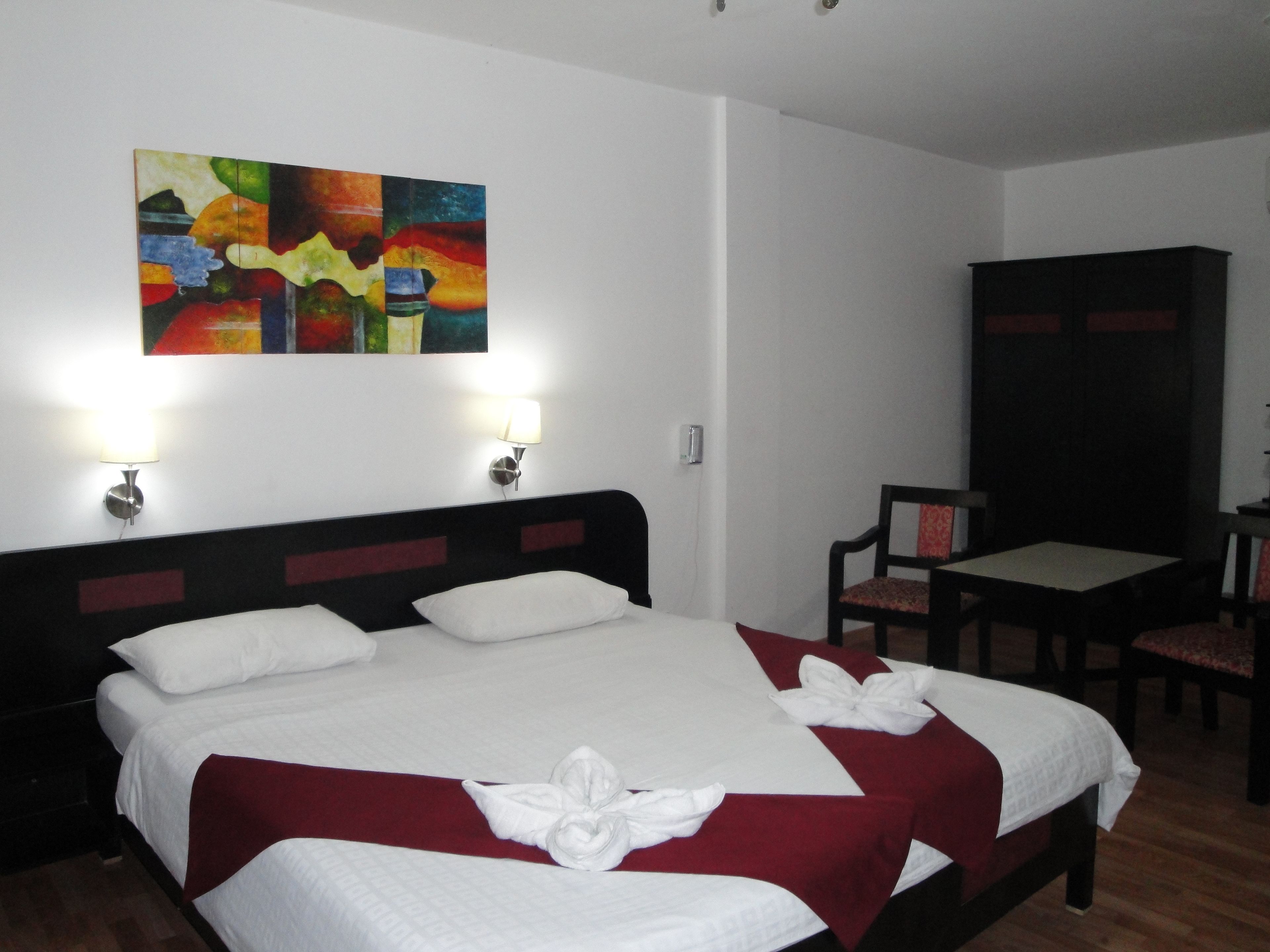 A hotel room with a large bed, two bedside lamps, a painting on the wall, a desk with a chair, and a wardrobe.