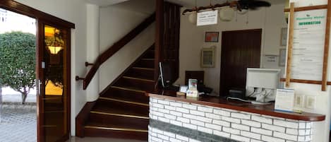 Zona de recepción de un hotel, con mostrador, escalera y letrero de recepción.
