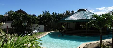 A swimming pool with lounge chairs, a covered pavilion, and lush greenery.
