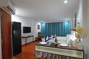 A hotel room with a dining area, a TV, a flat-screen TV, a desk, a chair, a bed, a window with curtains, and a vase with flowers. - Harmony Hotel (Panglao)