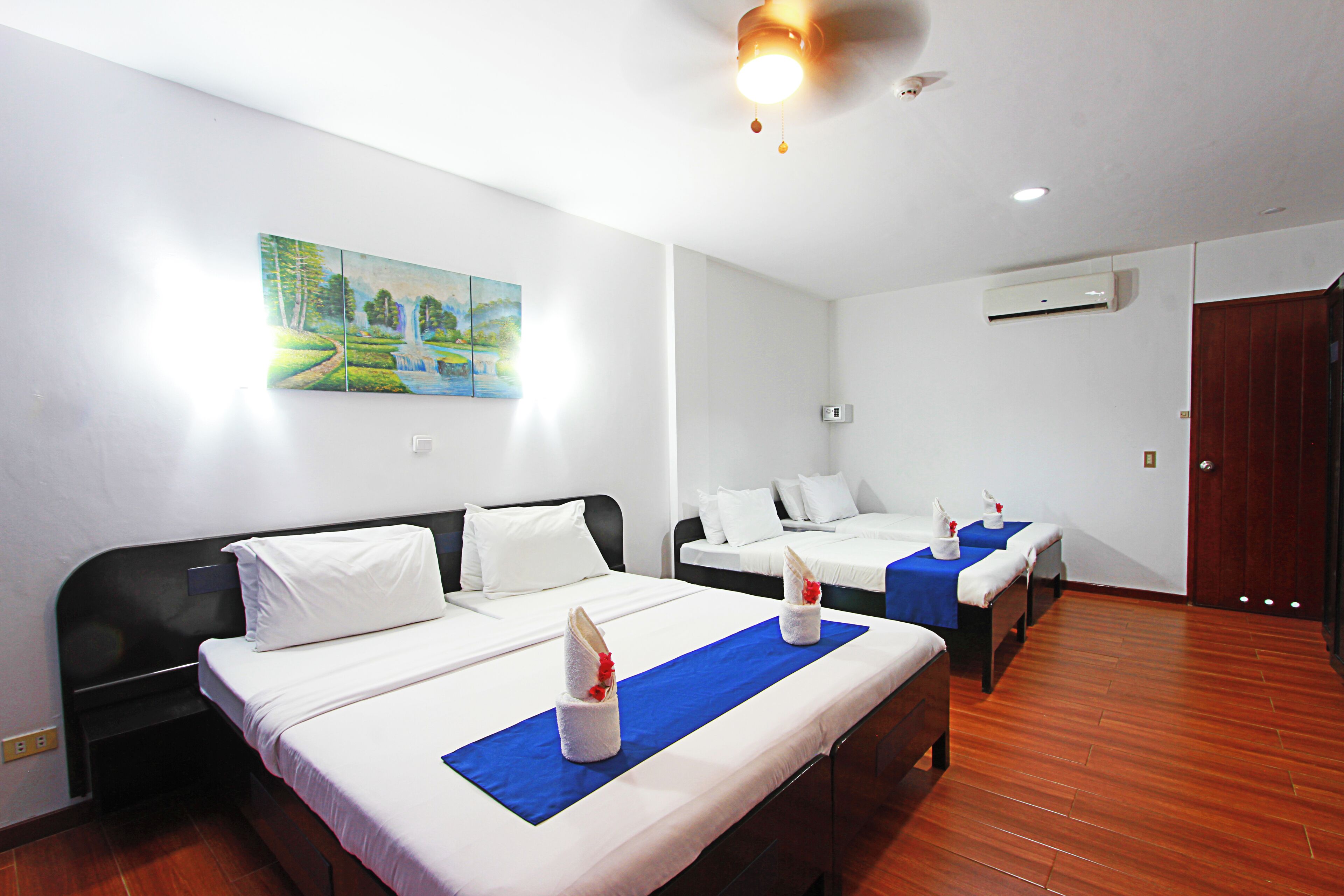 A hotel room with two beds, a painting on the wall, and an air conditioning unit.