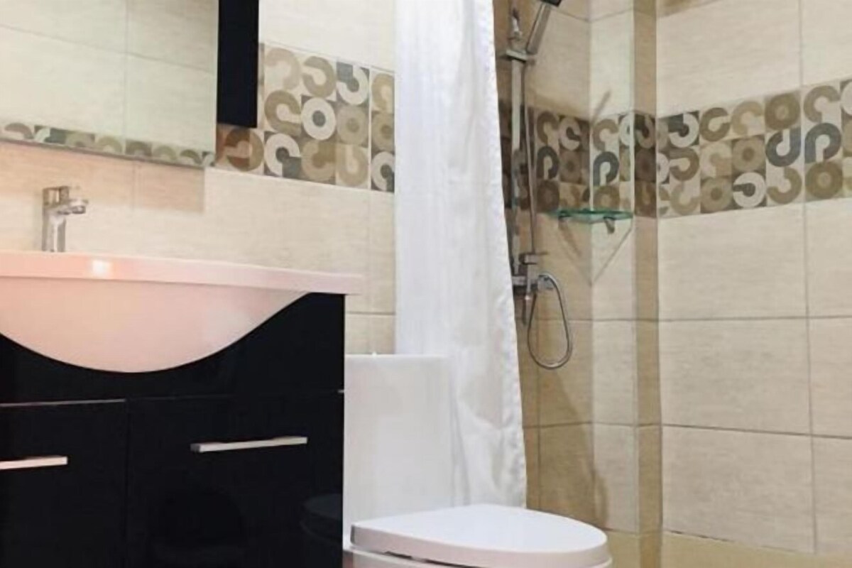 A bathroom with a white sink, black cabinets, a white toilet, and a shower area.