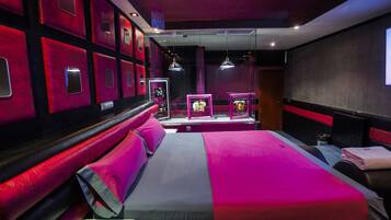 Habitación de hotel con una cama grande, zona de estar con una decoración en rojo y negro, y cuadros enmarcados en las paredes.