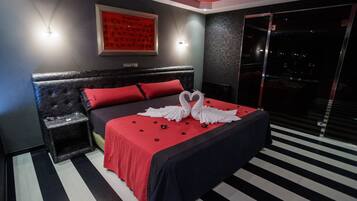 Una habitación de hotel moderna con una cama grande, ropa de cama roja y negra, una mesita de noche y una obra enmarcada en la pared.