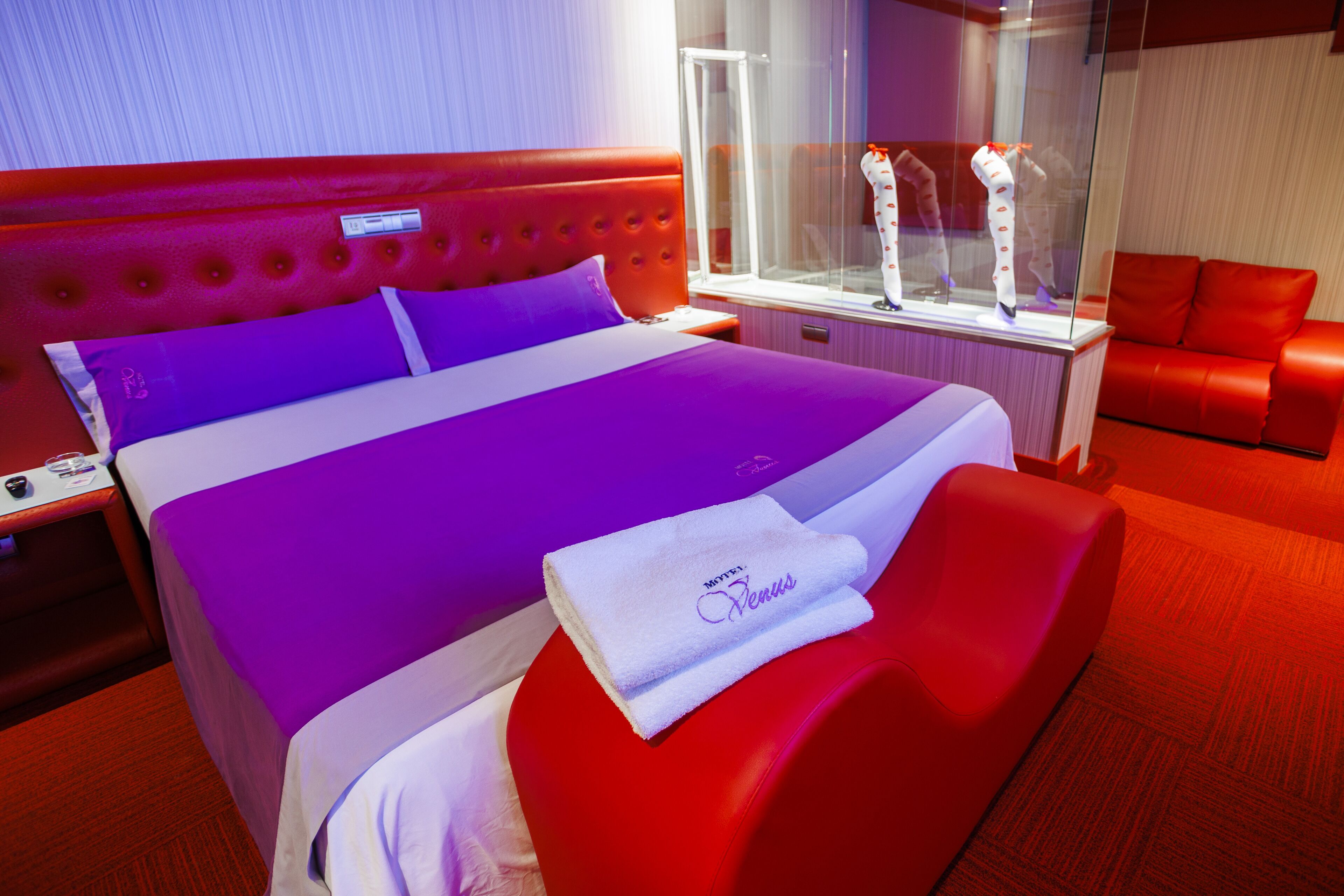 Habitación de hotel con una cama grande, ropa de cama roja y púrpura, una vitrina de vidrio y muebles rojos.