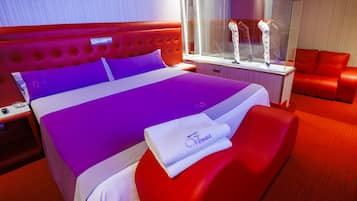 Habitación de hotel con una cama grande, ropa de cama roja y púrpura, una vitrina de vidrio y muebles rojos.