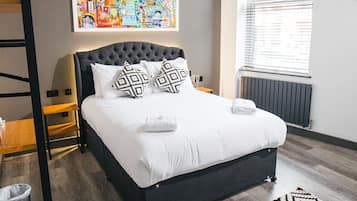 Ein modernes Schlafzimmer mit einem großen Bett, einem schwarzen Kopfteil, einem gemusterten Teppich und einem Fenster mit Jalousien.