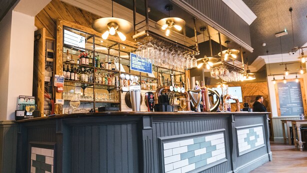 A bar area with a counter, shelves with bottles, and hanging lights. - The Black Lion Manchester (Salford)