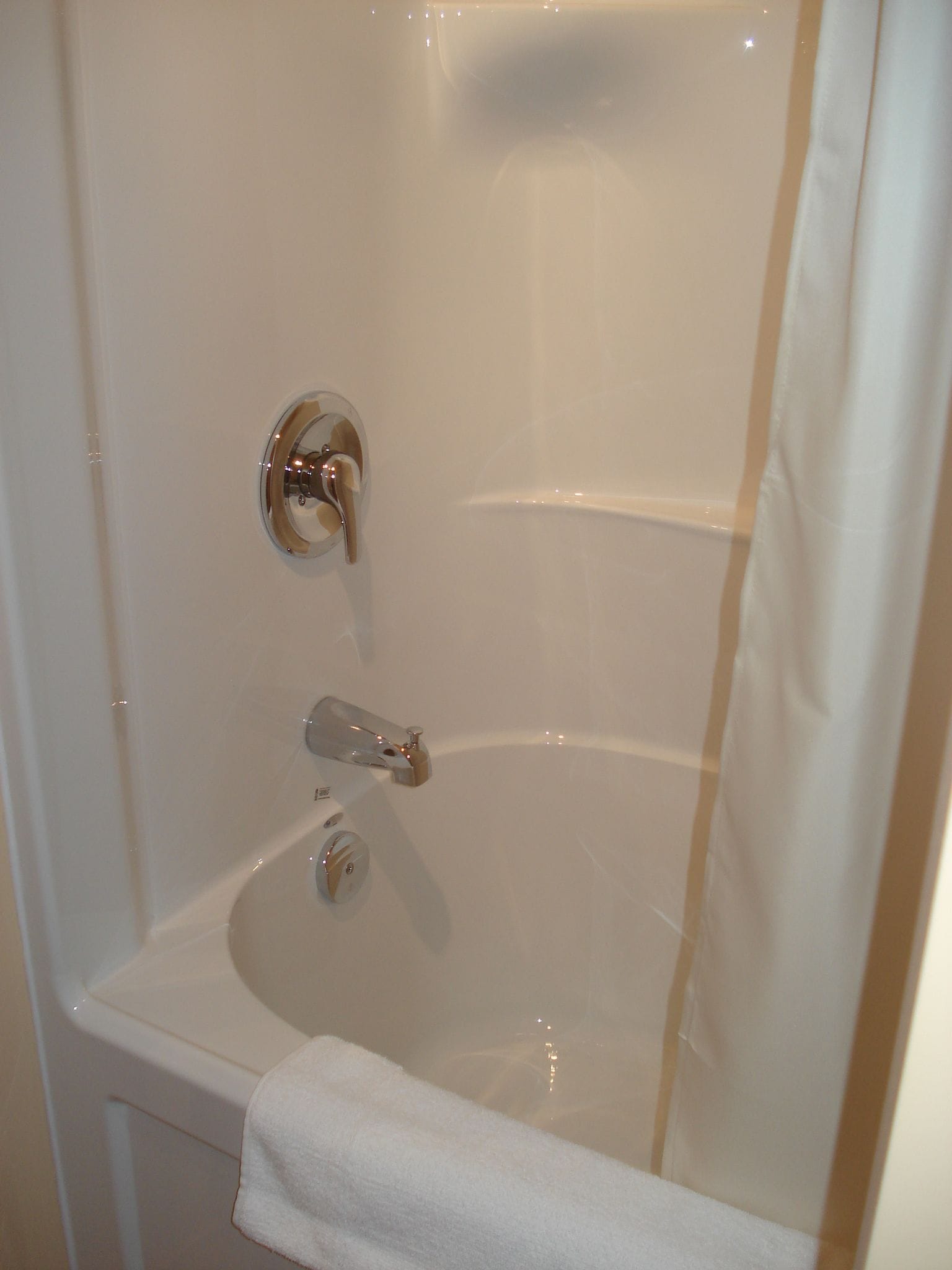 Una bañera blanca con accesorios cromados, una toalla y un cortinón de ducha.