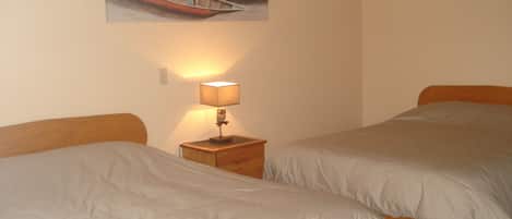 A hotel room with two beds, a nightstand with a lamp, and a painting of boats on the wall.