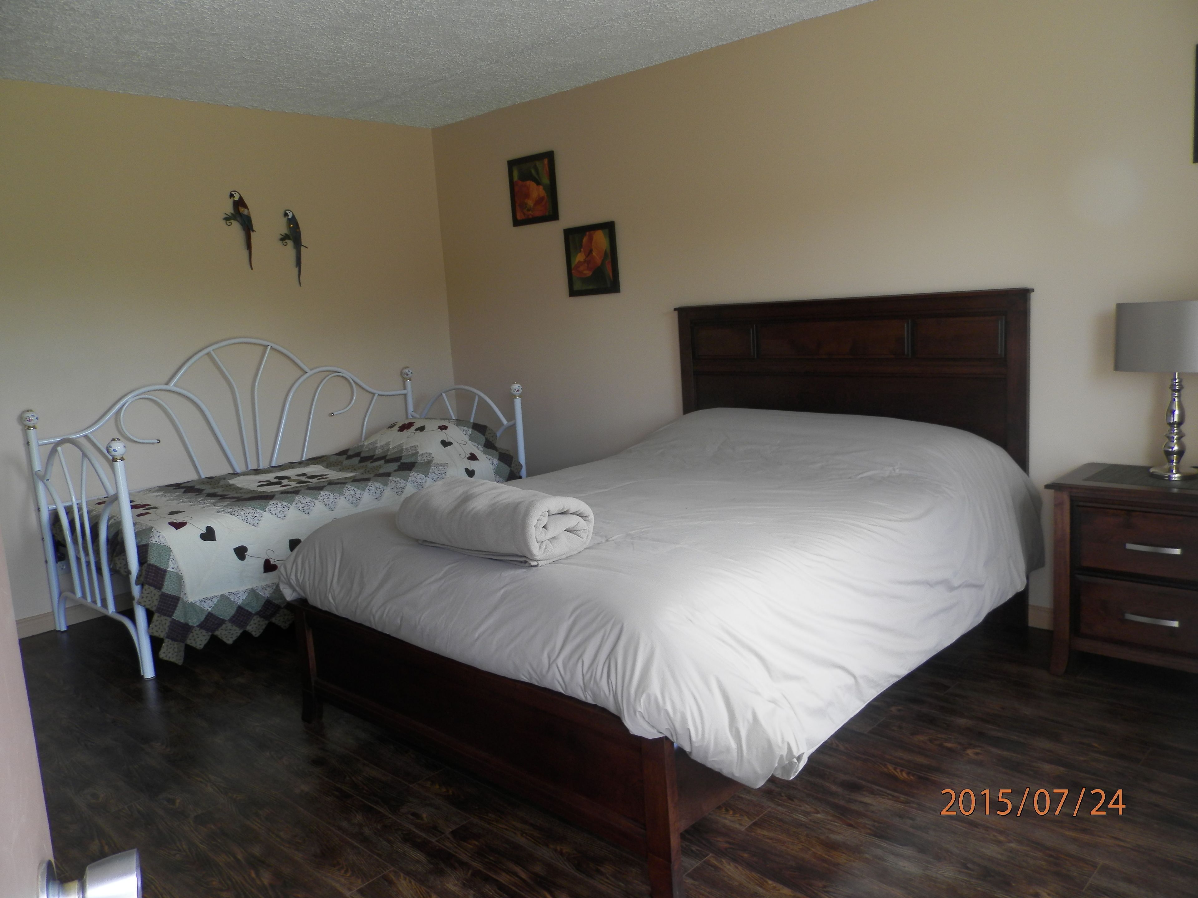 Une chambre à coucher avec un lit en bois, une tête de lit en métal, une table de chevet avec une lampe et un mur orné de deux tableaux encadrés.