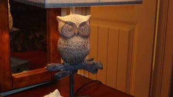 A lamp with an owl base and a rectangular shade, placed on a wooden table with a placard underneath.