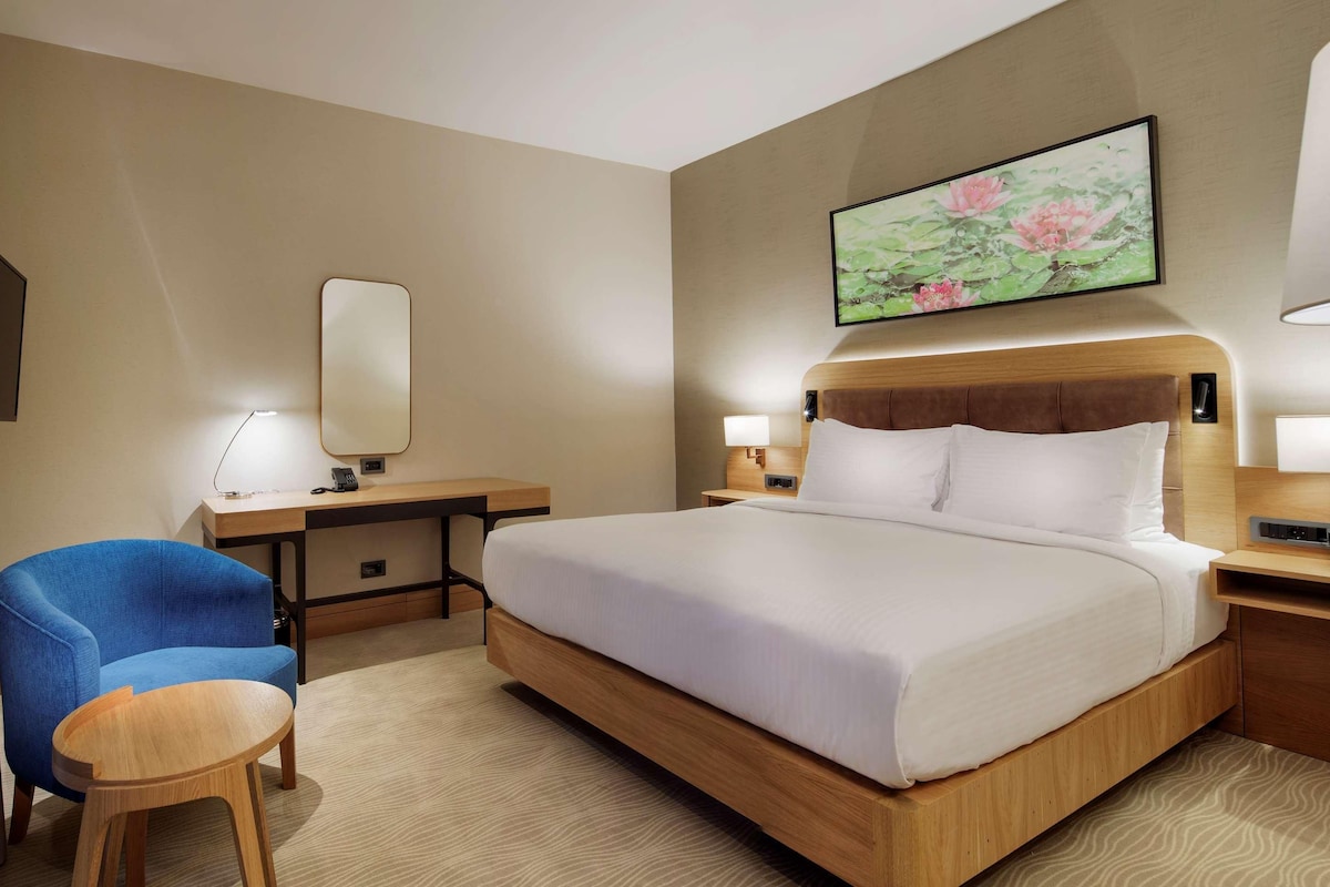 A hotel room with a large bed, a desk, a chair, and a bedside table.