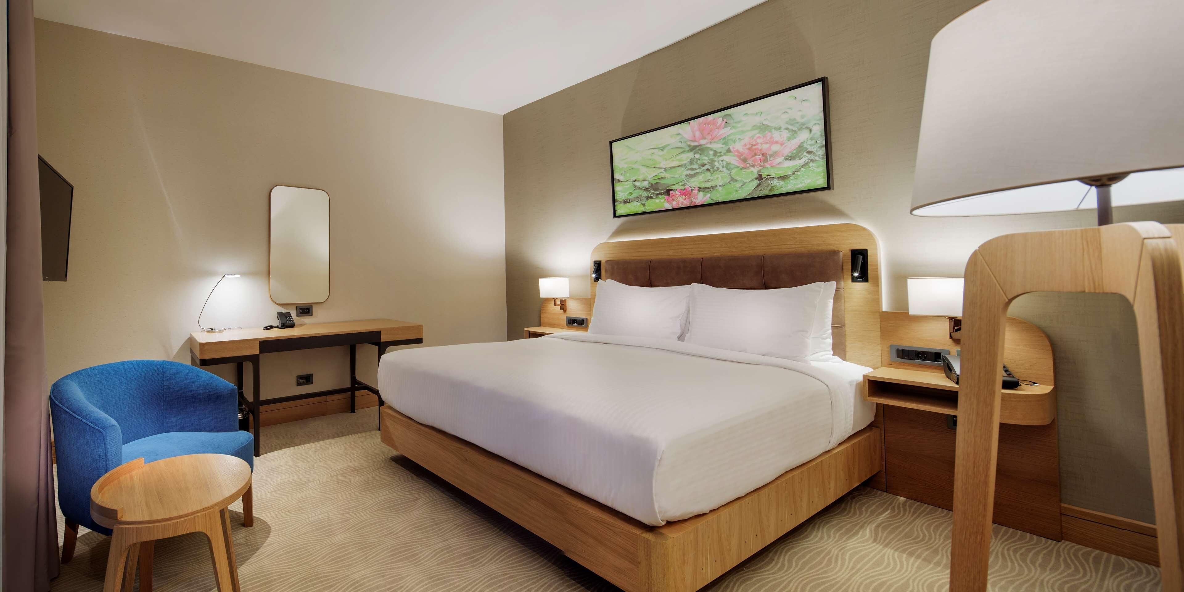 A hotel room with a large bed, a desk, a chair, and a bedside table.