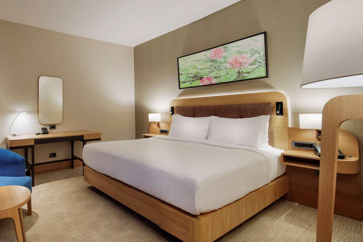 A hotel room with a large bed, a desk, a chair, and a bedside table.