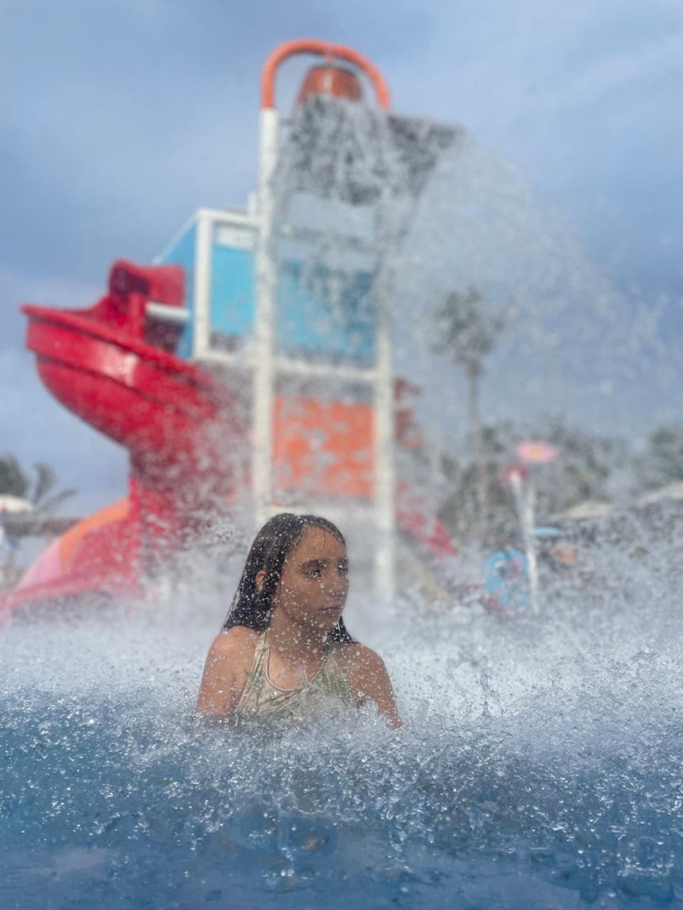 A person in a water play area with a water slide and a water pump in the background.