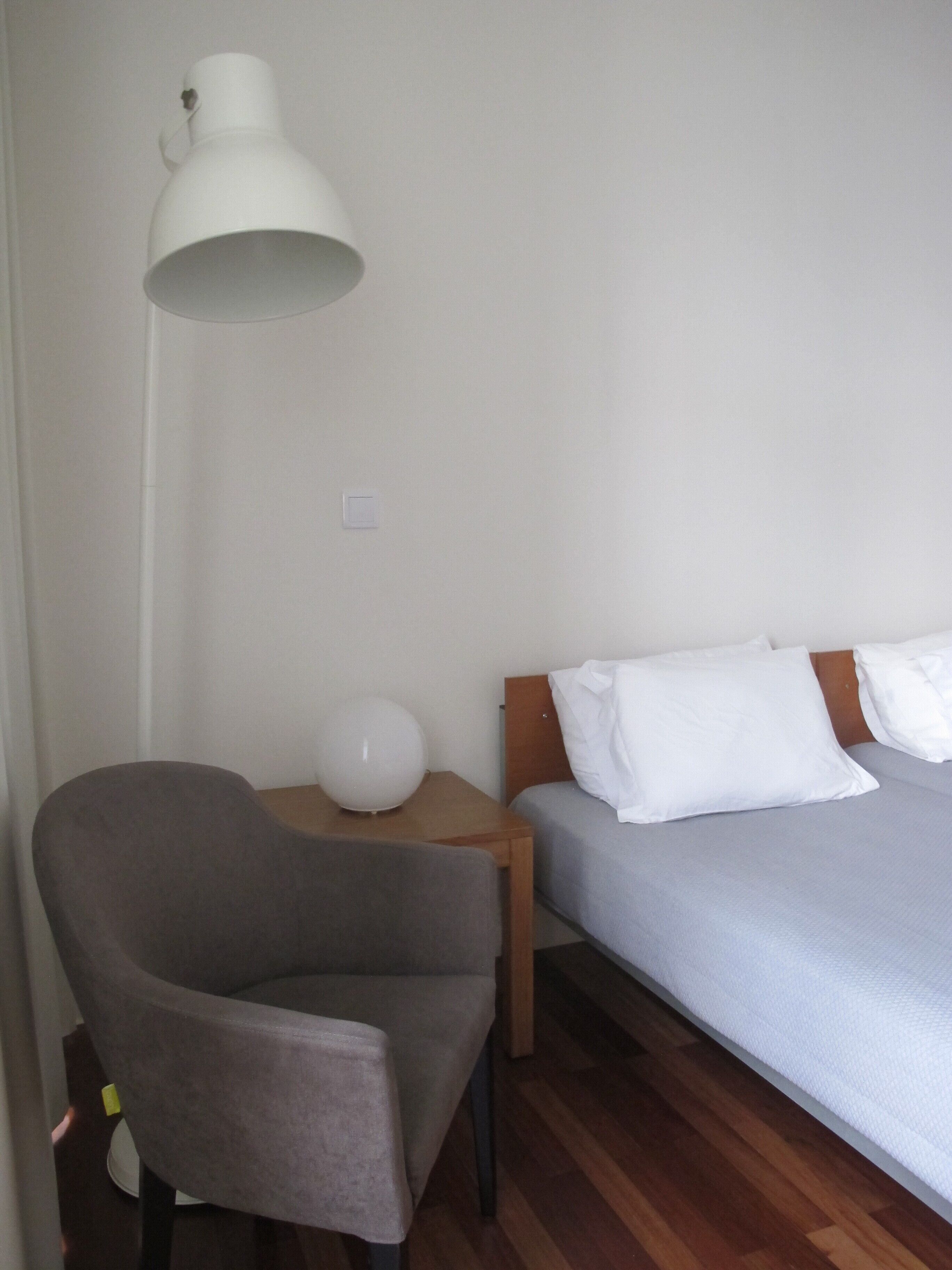 A bedroom with a bed, a chair, a bedside table, and a lamp.