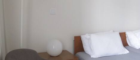 A bedroom with a bed, a chair, a bedside table, and a lamp.