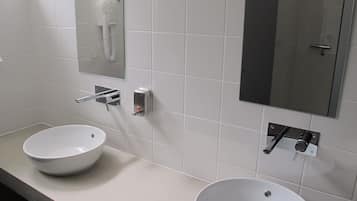 A bathroom with two white sinks, a mirror, and a hand dryer.