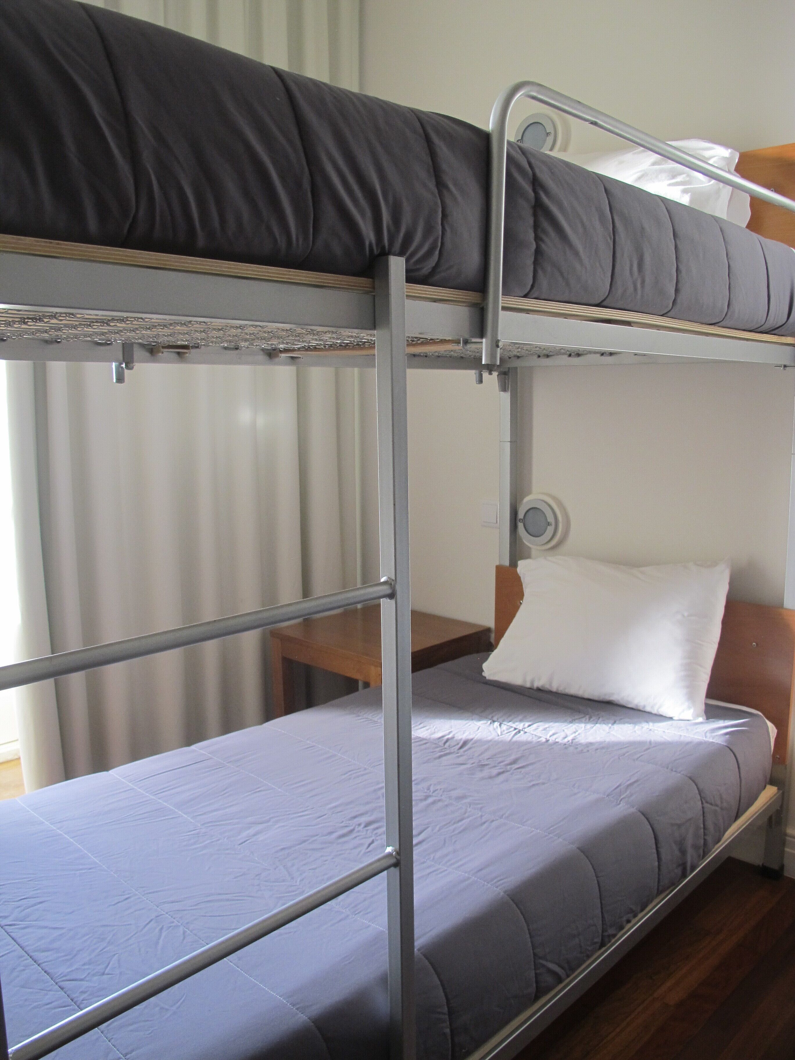 A bunk bed with a grey mattress and a pillow on the lower bunk.