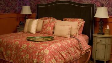 Un lit recouvert d’une couvre-lit à motifs floraux, une table de chevet avec une lampe et une petite table de nuit avec un téléphone.