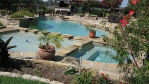A swimming pool with a red-roofed gazebo, surrounded by stone steps and potted plants.