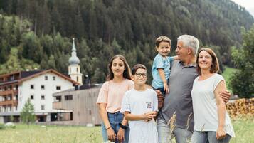 A family standing in a field with a building and forest in the background.